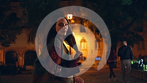 Girl strolling night city alone looking camera close up. Woman walking dark town