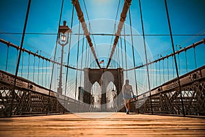 Girl strolls along the Brooklyn Bridge in New York City at sunset