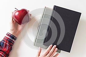 Girl student holding apple. Books on white table