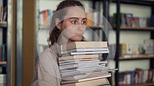 Girl student holding a lot of books in the library, preparing for exams