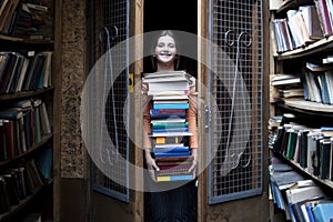 Girl student holds a large stack of books and carries a lot of literature in the library, she is preparing for study, the seller