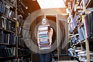 Girl student holds a large stack of books and carries a lot of literature in the library, she is preparing for study, the seller