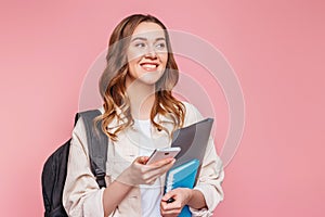 Girl student laughing and looking away and holding a mobile phone isolated on a pink background, copy space. Young woman with