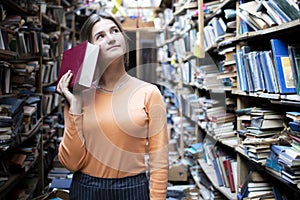 Girl student reads a book in the library, a woman likes to read a lot, she is looking for literature on bookshelves, knowledge is