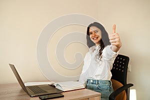 Girl student showing thumbs up. Schoolgirl with laptop done homework online and gesturing thumbs up at table at home.