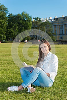 Girl-student sit on lawn and reads textbook.