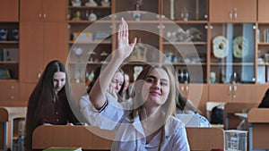 A girl student sitting at a desk raises her hand in the class.