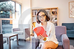 Girl student with stylish glasses reading books in the library