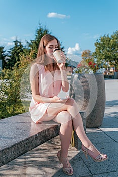 Girl student summer city sits bench autumn spring, wears pink dress, reads writes message smartphone, drinks coffee tea