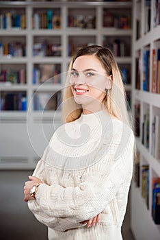 Girl student in the university library, in the background shelves with books.