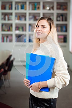 Girl student in the university library, in the background shelves with books.