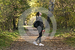 Girl student walks in the autumn park. Stylish young woman walks in the forest. Alley with yellow fallen leaves