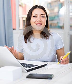 Girl student working with laptop and pen at table in home