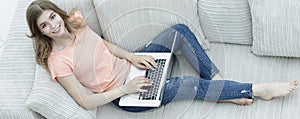 Girl student working with laptop sitting on sofa and looking at camera.