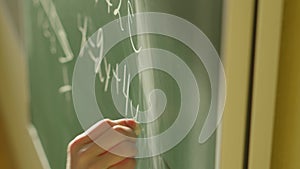 A girl student writes on a green board. Female teacher near school board. hand writes information