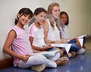 Girl, students and portrait of friends with books sitting at school in hallway for education or learning. Group of young