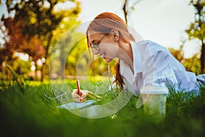 girl studies, works on laptop, blogger, makes notes, distance education while lying on the grass