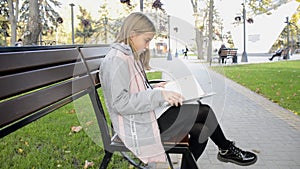 girl studying a book in English on a bench in a city park. additional education