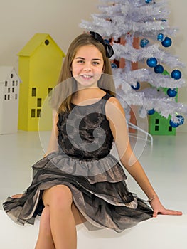 Girl in Stylish Dress Sitting on the Floor in Front of Christmas Tree.