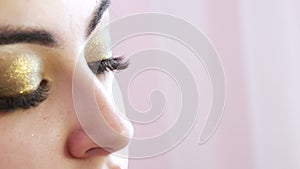 Girl stylist make-up make-up artist applies a thin line of black eyeliner on shiny make-ups in gold tones on the model's