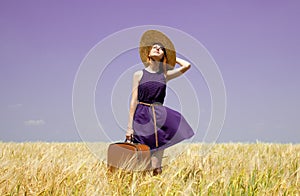 Girl with suitcase at spring wheat field.