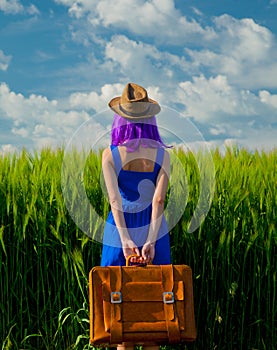 Girl with suitcase standing at wheat field