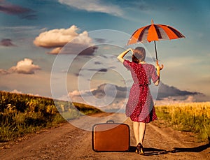 Girl with suitcase and umbrella waking on road