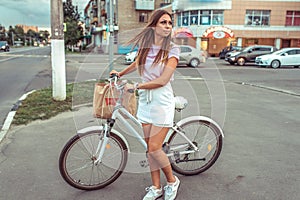 The girl in summer city crossroads, stands with bicycle and package. Waiting for a free road to go. Concept woman after