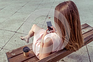 Girl in summer in city sits on sky-bike. In hands of phone is an on-line application of personal networks, cup of coffee