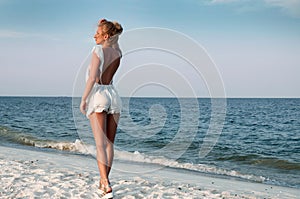Girl in summer dress standing on a beach and looking to the sea