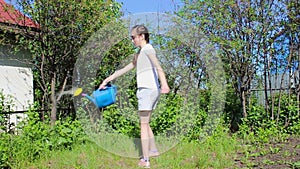 A girl in the summer garden on a Sunny day turns around with a watering can and waters the lawn.