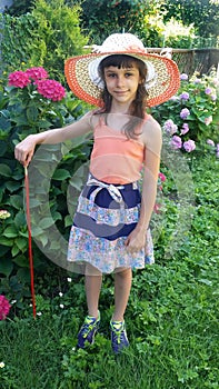 The girl in a summer hat stands near a bush of the blossoming hydrangea on the seasonal dacha