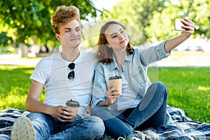 With a girl in summer in nature. They sit on a blanket. He holds cups with coffee or tea in his hands. He takes pictures