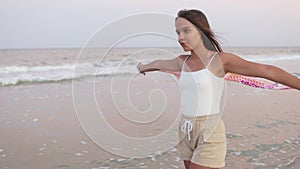 A girl in a summer T-shirt and shorts is walking along the beach looking at the horizon and holding a shawl in her hands