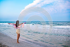 A girl in a summer T-shirt and shorts is walking along the beach looking at the horizon and holding a shawl in her hands