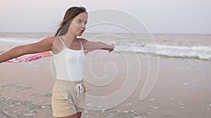 A girl in a summer T-shirt and shorts is walking along the beach looking at the horizon and holding a shawl in her hands