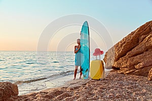 Girl on summer trip, suitcase and hat on sand. Board for sea surf. Idea of summer time, desire of adventure, copy space