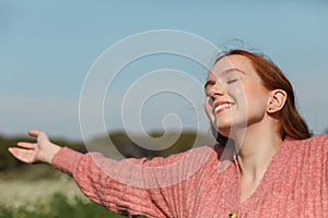 Girl sunbathes in the spring sun with her eyes closed and arms outstretched