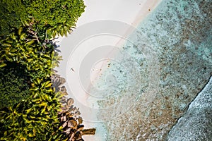 Girl sunbathing on tropical cocos beach with beautiful rocks, palm trees and ocean waves. Aerial drone shot. Seychelles