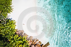 Girl sunbathing on tropical sandy beach surrounded by brown rocks, coconut palm trees and turquoise azure ocean lagoon