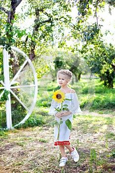 Girl with a sunflower. Happy child with walks in the garden. Portrait of a charming little girl with a sunflower. The concept of c