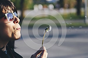 Girl with sunglases blowing a dandelion