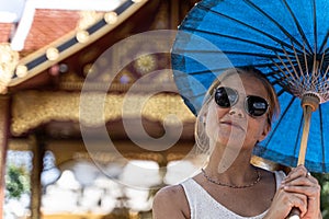 Girl with sunglasses and a blue umbrella in her hands with a happy expression in front of a temple