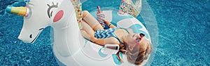 Girl in sunglasses with drink lying on inflatable ring unicorn. Kid child enjoying having fun relaxing in swimming pool on floatie