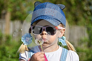 A girl in sunglasses in the field is blowing strongly at a flower dandelion, close-up, summer