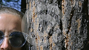 Girl in sunglasses, leaning against a tree, looks thoughtfully. Close up