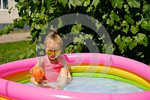 Girl splashes in a small inflatable round swimming pool next to the house