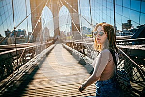 Girl in sunglasses strolls along the Brooklyn Bridge in New York City at sunset