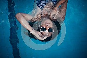 A girl in sunglasses swims in the pool. Beautiful woman resting in the water in the outdoor pool