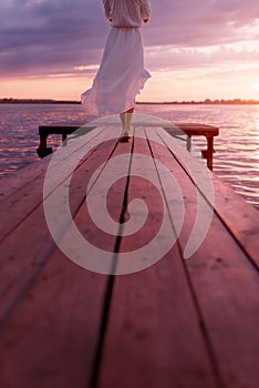 A girl in the sunset light walks along a wooden bridge